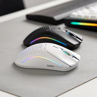 A white Glorious Model O 2 Wireless gaming mouse with RGB lighting is placed in front of a black Model O 2 Wireless on a mousepad.